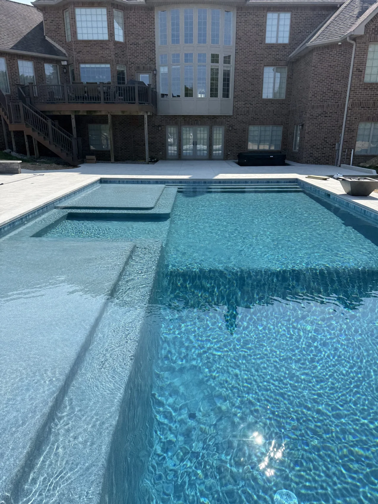 Gunite pool with a raised spa and shallow sun shelf beside a brick home